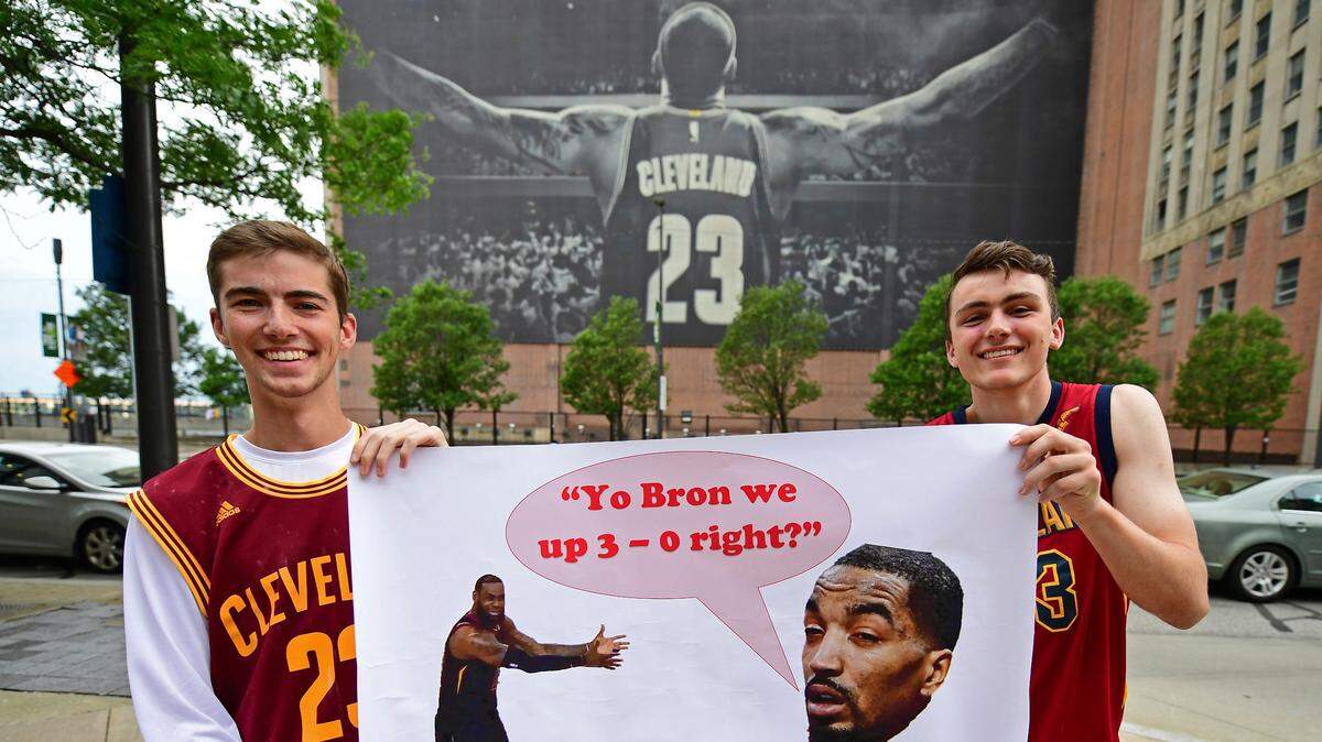 Dos hinchas de los Cavaliers posan con un cartel delante de la gran pancarta de LeBron James en el centro de Cleveland.