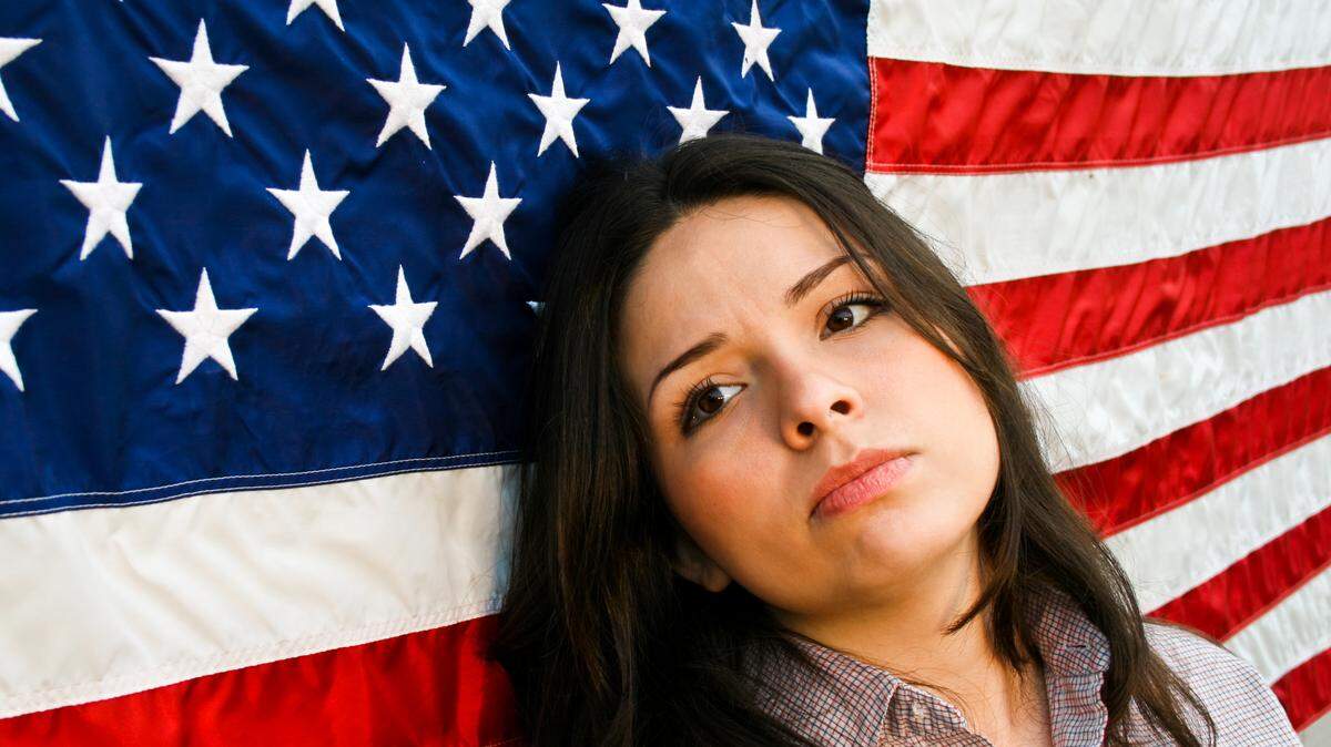 Representación artística de una mujer latina desilucionada recostada sobre una bandera de Estados Unidos. Inmigrantes, empresarios, abogados y representantes autorizados pueden preparar y presentar una solicitud de asistencia de caso ante el CIS Ombudsman.