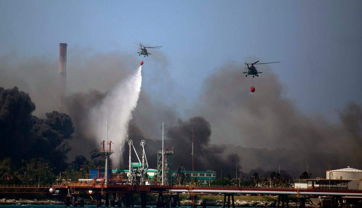 Helicópteros que transportan agua sobrevuelan la base de Supertanqueros de Matanzas mientras bomberos y especialistas trabajan para sofocar el incendio que comenzó durante una tormenta eléctrica en Matanzas, Cuba, el lunes 8 de agosto de 2022.