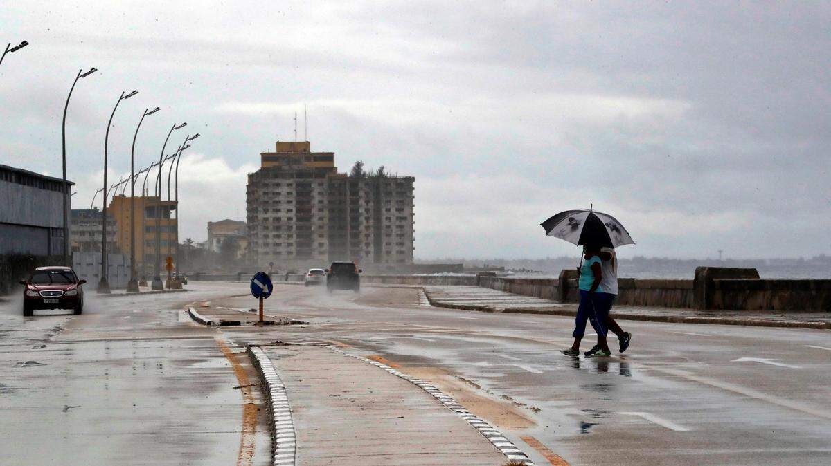 Foto de archivo del 8 de noviembre de 2020 que muestra a dos personas protegiéndose de la lluvia mientras cruzan el Malecón de La Habana. El miércoles 13 de diciembre de 2023, el Instituto Nacional de Meteorología alertó de fuertes lluvias en la capital de Cuba.
