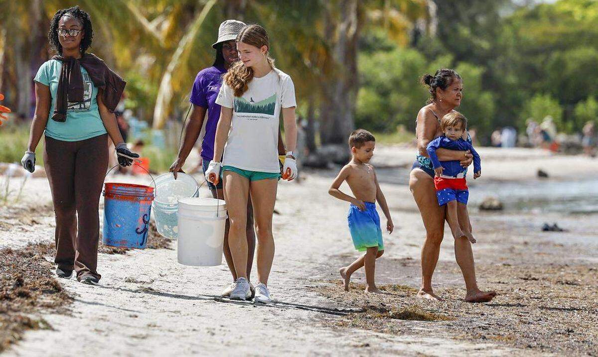Ethan Sims se une a su hija Zoe Sims, de 17 años, ambos de Boise, Idaho, durante una limpieza de playa en el viaducto Rickenbacker el viernes. Ella estaba allí para asistir a una importante conferencia sobre el clima para jóvenes en la Universidad de Miami.