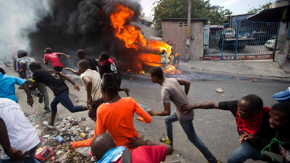 Los manifestantes huyen de la policía que está disparando en su dirección, mientras un automóvil se quema durante una protesta que exige la renuncia del presidente haitiano, Jovenel Moise, en Puerto Príncipe, Haití, el martes 12 de febrero de 2019. Los manifestantes están enojados por la creciente inflación. y el hecho de que el gobierno no haya procesado la malversación de un programa multimillonario de Venezuela que envió petróleo descontado a Haití. (Foto AP / Dieu Nalio Chery)