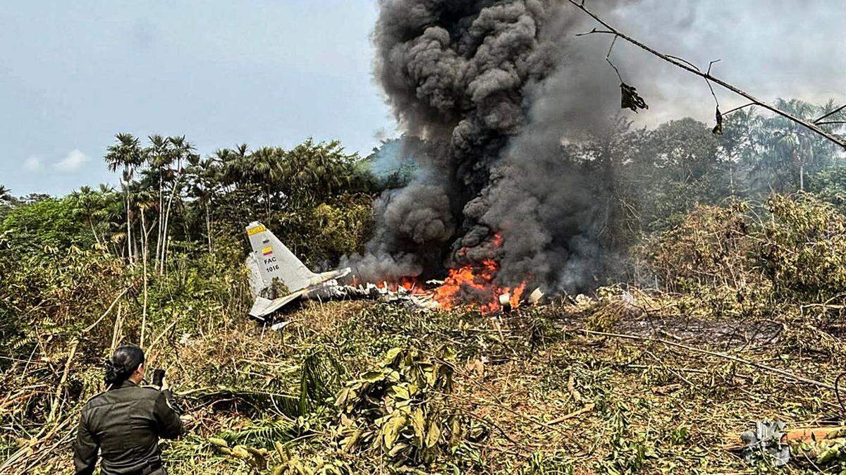 TOPSHOT - Flames and thick black smoke rise from an Air Force Hercules that crashed during takeoff, as a member of the Colombian Police stands nearby, in Puerto Leguizamo, Colombia, near the southern border with Ecuador, on March 23, 2026. Colombia's military said on March 23 that about 80 troops were believed to be dead after a transport plane crash in the south of the country. (Photo by daniel ortiz / AFP via Getty Images)