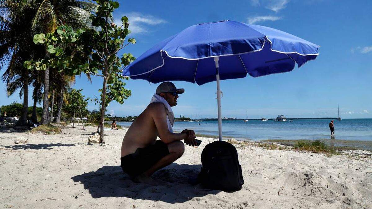 Michelangelo Manganelli sentado a la sombra de su sombrilla para evitar el ardiente sol en la playa del viaducto Rickenbacker, en Miami, Florida, el jueves, 6 de junio de 2024. 