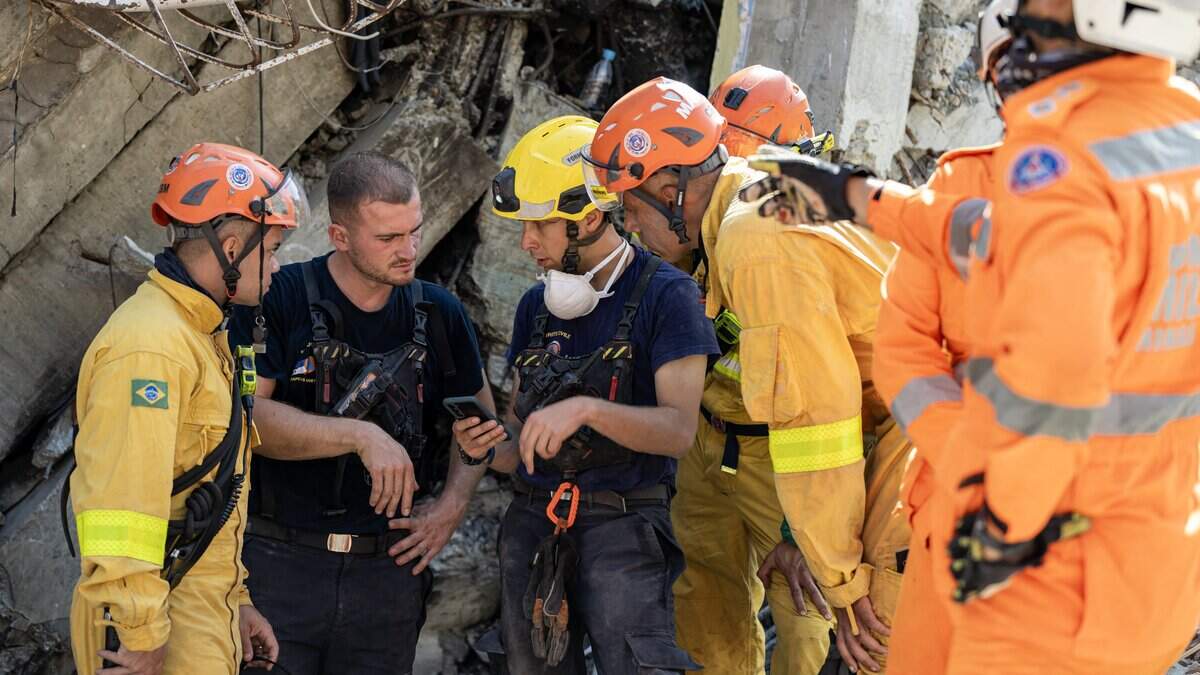 Members of the 7th Civil Security Training and Intervention Regiment exchange information with Brazilian rescue workers next to a damaged building in Catia La Mar, La Guaira state, Venezuela, on June 29, 2026. Hopes were fading on June 29, 2026 of finding survivors more than four days after powerful twin earthquakes struck Venezuela, as residents grow increasingly frustrated with the government's response to the disaster that has killed at least 1,450 people and left tens of thousands unaccounted for. (Photo by Miguel MEDINA / POOL / AFP via Getty Images)