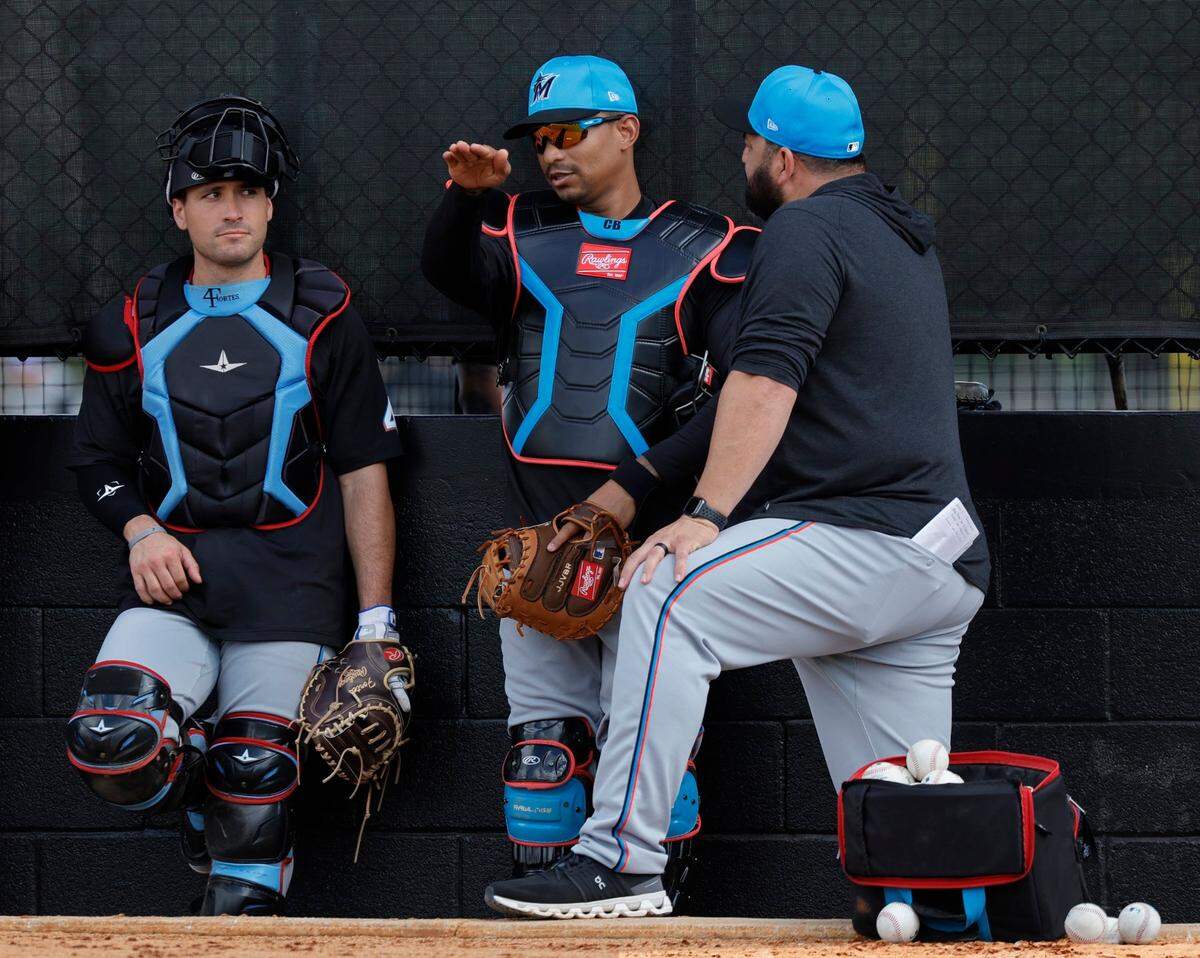Los receptores de los Marlins Nick Fortes (izq.) y Christian Bethancourt (centro) conversan con el coach Rod Barajas en el entrenamiento de primavera, el 15 de febrero de 2024 en Jupiter, Florida.