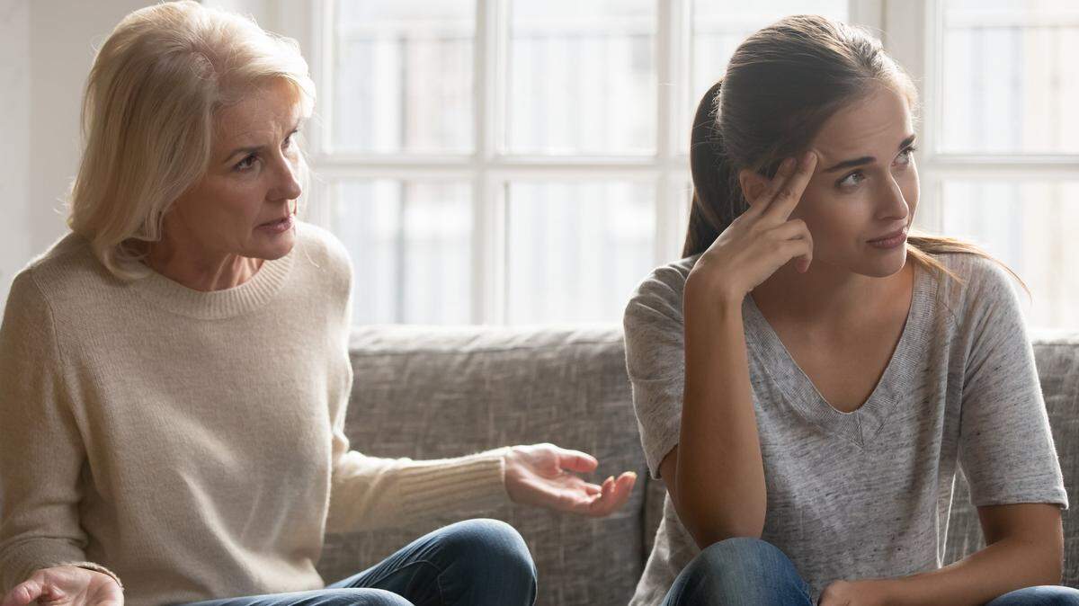 Tired annoyed millennial woman lose patience ignore senior anxious mom talking lecturing at home, elderly middle-aged authoritative mother sit on couch scolding moralizing grownup adult daughter