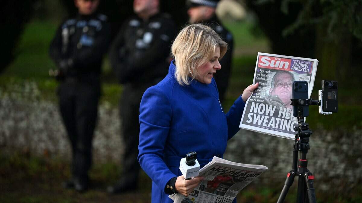 Una reportera informa desde el lugar mientras sostiene un periódico con la imagen del ex príncipe británico Andrés, en una de las entradas a Wood Farm, en la finca Sandringham de la familia real, en Norfolk, al este de Inglaterra, el 20 de febrero de 2026, un día después de que Andrew Mountbatten-Windsor fuera arrestado.