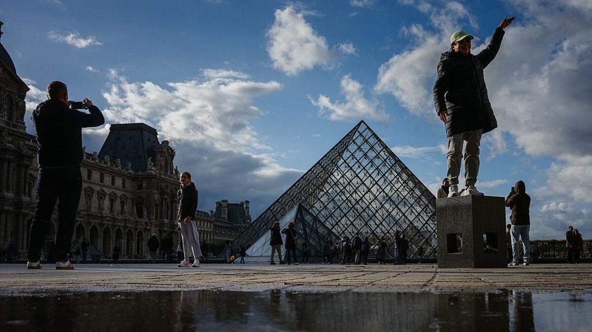 Guest Tourists pose for a photo in front of the Pyramide du Louvre, designed by Chinese-US architect Ieoh Ming Pei, with the Louvre Museum in the background in Paris on October 23, 2025. The Louvre Museum reopened its doors to visitors in the morning of October 22, 2025 for the first time since the spectacular robbery on October 19, 2025 by four criminals, who made off with eight jewels worth an estimated 88 million. (Photo by Dimitar DILKOFF / AFP) / RESTRICTED TO EDITORIAL USE - MANDATORY MENTION OF THE ARTIST UPON PUBLICATION - TO ILLUSTRATE THE EVENT AS SPECIFIED IN THE CAPTION (Photo by DIMITAR DILKOFF/AFP via Getty Images)