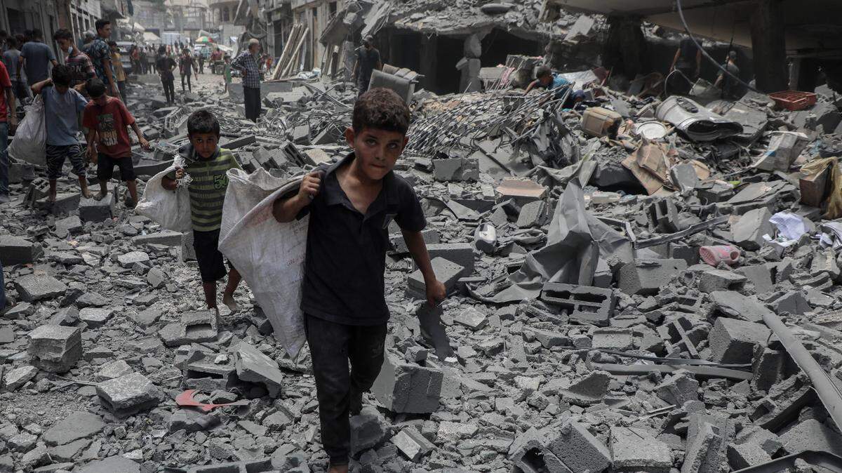 Niños llevan objetos recolectados caminan sobre escombros tras un ataque aéreo israelí en la ciudad de Gaza el 8 de agosto de 2025.