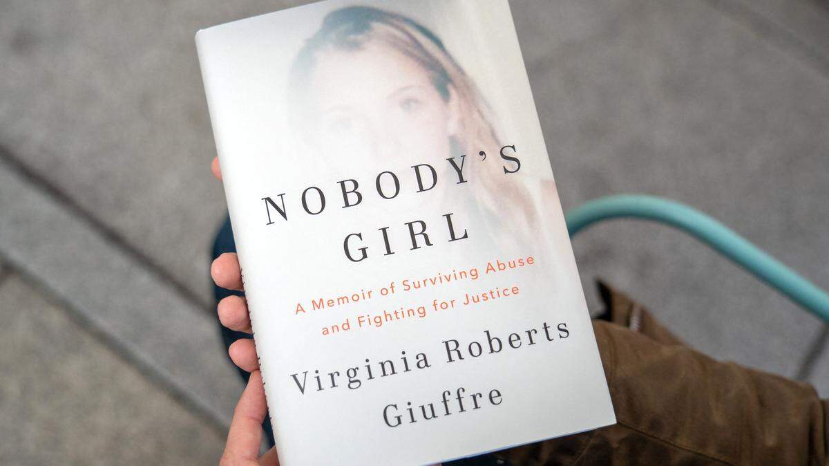 A person poses for a photo with a copy of the book "Nobody's Girl - A Memoir of Surviving Abuse and Fighting for Justice" by Virginia Roberts Giuffre, in central London on October 21, 2025, on the day of its release in the UK. A memoir by one of Jeffrey Epstein's main accusers whose claims led to the downfall of Britain's Prince Andrew was released Tuesday, promising to keep Epstein's ties to President Donald Trump in the spotlight. (Photo by Niklas HALLE'N / AFP) (Photo by NIKLAS HALLE'N/AFP via Getty Images)