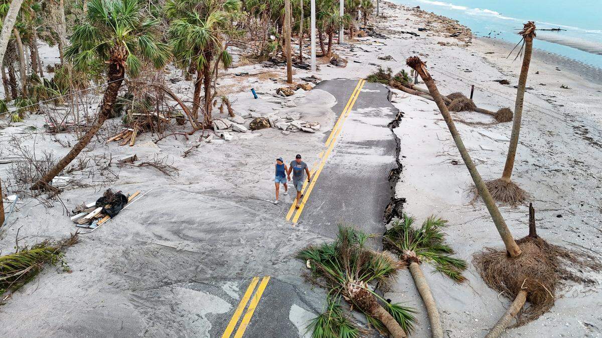 Anna y Alex Marchuk, de izquierda a derecha, caminan por una carretera arrasada de Manasota Key el viernes 11 de octubre de 2024. Los extensos daños fueron causados ​​por los huracanes Helene y Milton en Manasota Key, Florida.
