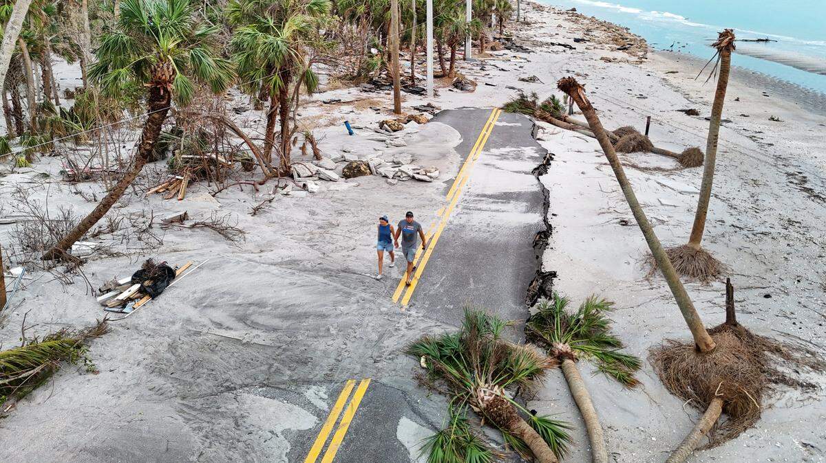Anna y Alex Marchuk, de izquierda a derecha, caminan por una carretera arrasada de Manasota Key el viernes 11 de octubre de 2024. Los extensos daños fueron causados ​​por los huracanes Helene y Milton en Manasota Key, Florida.
