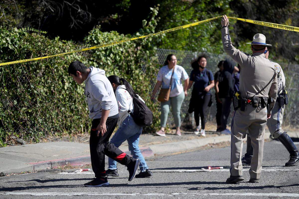 Un oficial de la Patrulla de Carreteras de California levanta la cinta policial para permitir que los padres y los estudiantes abandonen un área acordonada en Fountain Street, luego de un tiroteo en un campus escolar en Oakland, California, el miércoles 28 de septiembre de 2022.