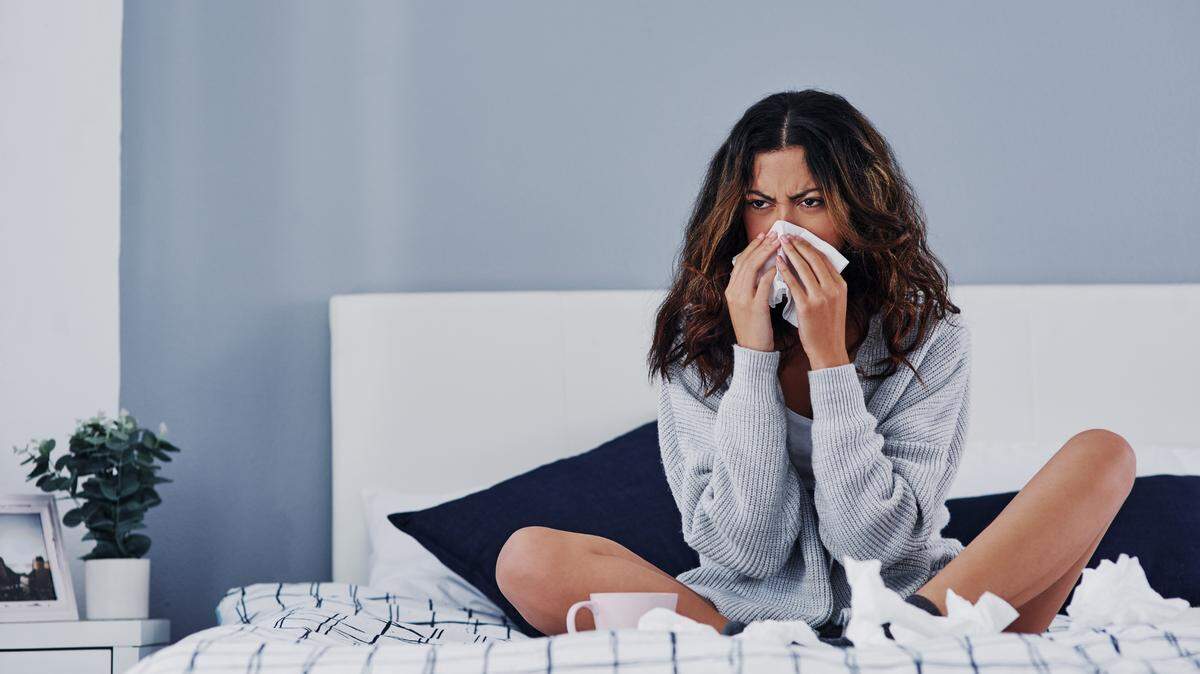 Full length shot of an attractive young woman sitting at home and blowing her nose while suffering from a cold