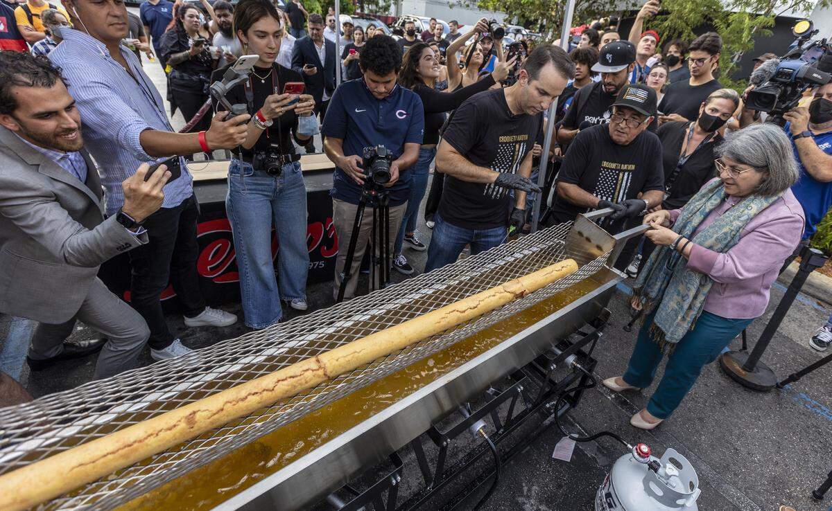 Con ayuda de un empleado de Sergio’s, la alcaldesa del condado de Miami-Dade, Daniella Levine Cava, levanta ligeramente una croqueta gigante del aceite caliente mientras el director ejecutivo de Sergio’s, Carlos Gazitua, les dirige.