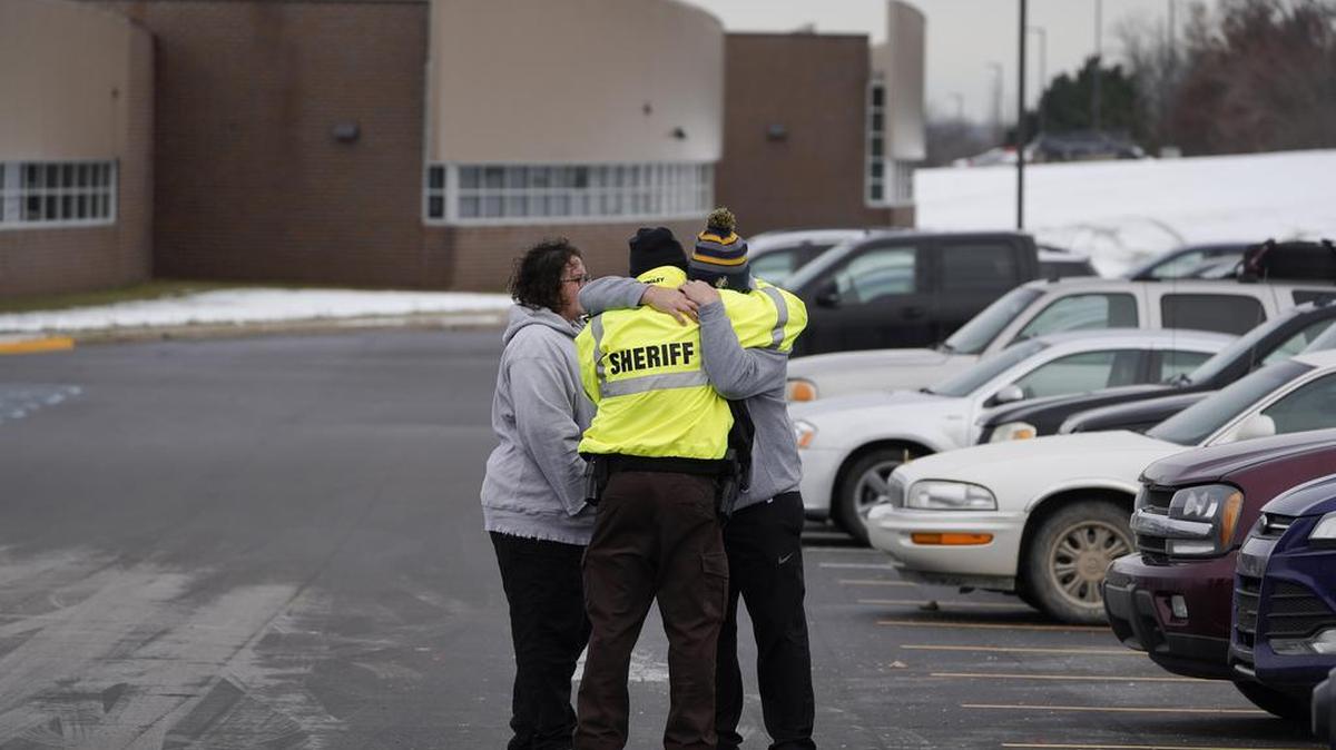 Un policía del condado de Oakland abraza a los familiares de un estudiante en el estacionamiento de Oxford High School en Oxford, Michigan, el miércoles 1 de diciembre de 2021. AP / Paul Sancya