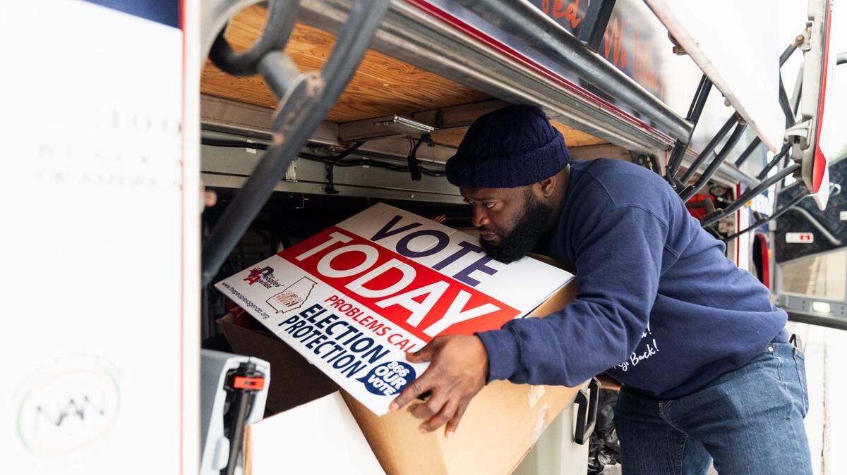 Sean Floyd, de la Coalición Nacional para la Participación Cívica de la Comunidad Negra, ayuda a cargar letreros en un autobús antes de que él y otros voluntarios se dirijan al condado de Clayton para recorrer la zona y alentar a las personas a votar en las elecciones el lunes 4 de noviembre de 2024