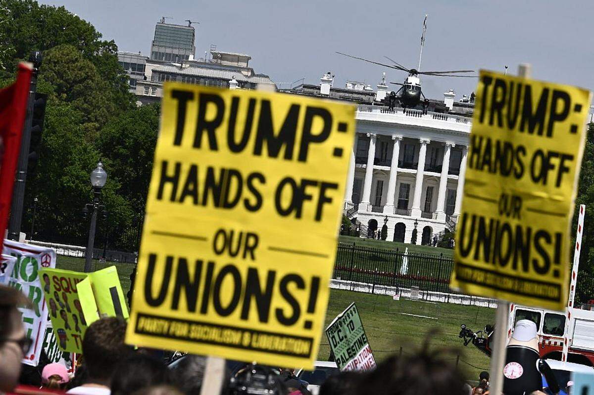 Manifestantes sostienen pancartas durante una concentración del Primero de Mayo, conmemorando el Día Internacional de los Trabajadores, mientras el Marine One —con el presidente estadounidense Donald Trump a bordo— despega desde el Jardín Sur de la Casa Blanca en Washington, D. C., el 1 de mayo de 2026. Trump se dirige a Florida para hablar en un evento en The Villages y asistir a la cena del Forum Club of the Palm Beaches.
