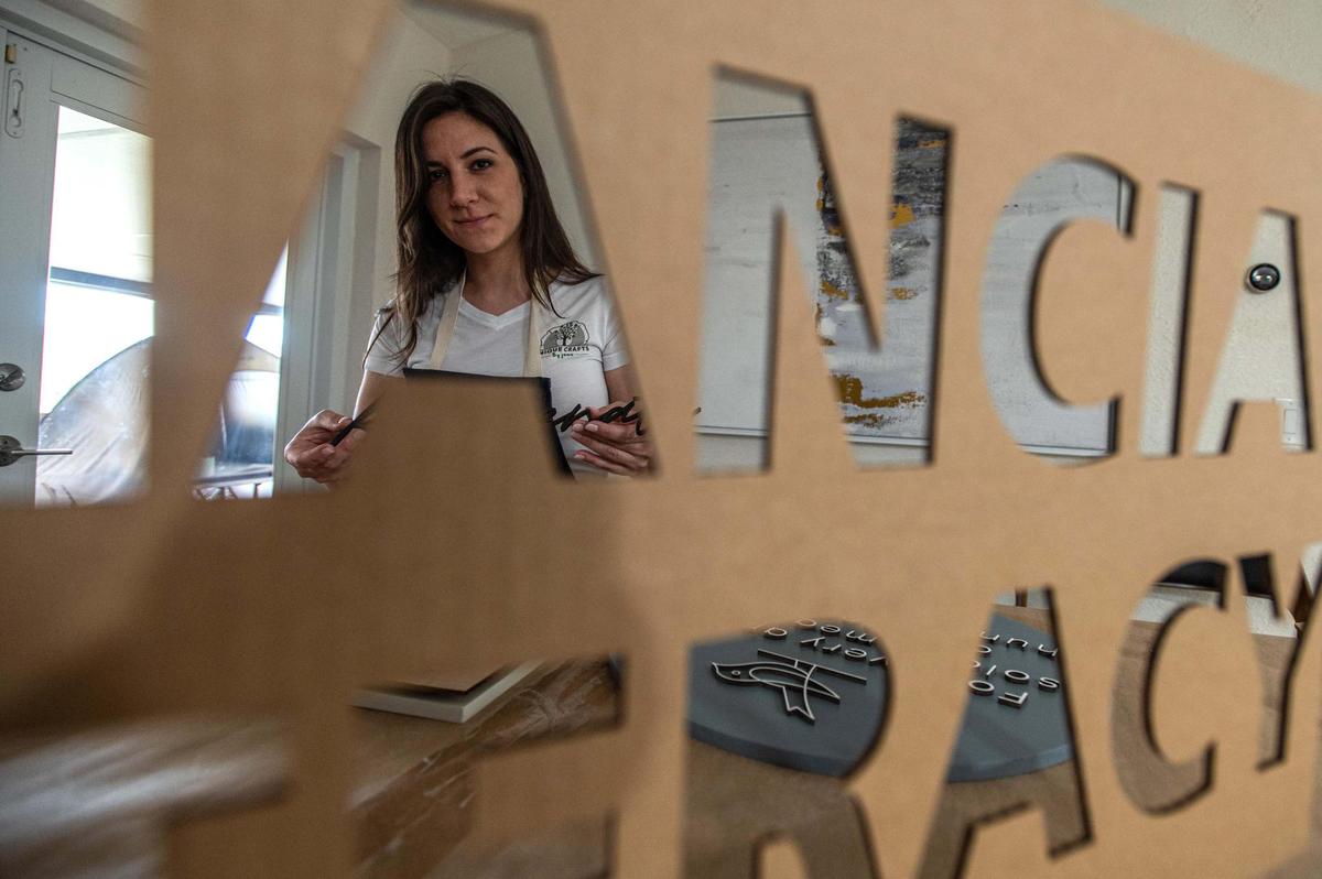 Jennifer Arniella se ve a través de una de las plantillas que emplea para hacer los letreros en su negocio, que lanzó hace un año en su casa en el suroeste de Miami.