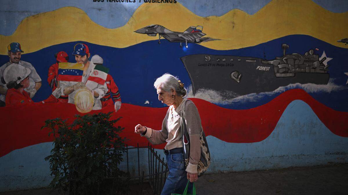 Una mujer camina frente a un mural de un buque de guerra y aviones militares de Venezuela en una calle de Caracas, el 26 de diciembre de 2025.