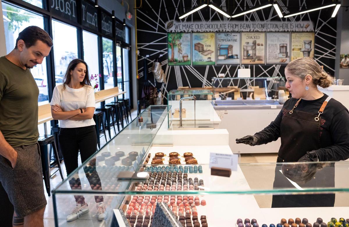 Carolina Quijano, a la derecha, fundadora de Exquisito Chocolates, conversa con los clientes Gabriel Gasparini y Laylla Florez mientras deciden qué pedir en la nueva fábrica de la Calle Ocho.