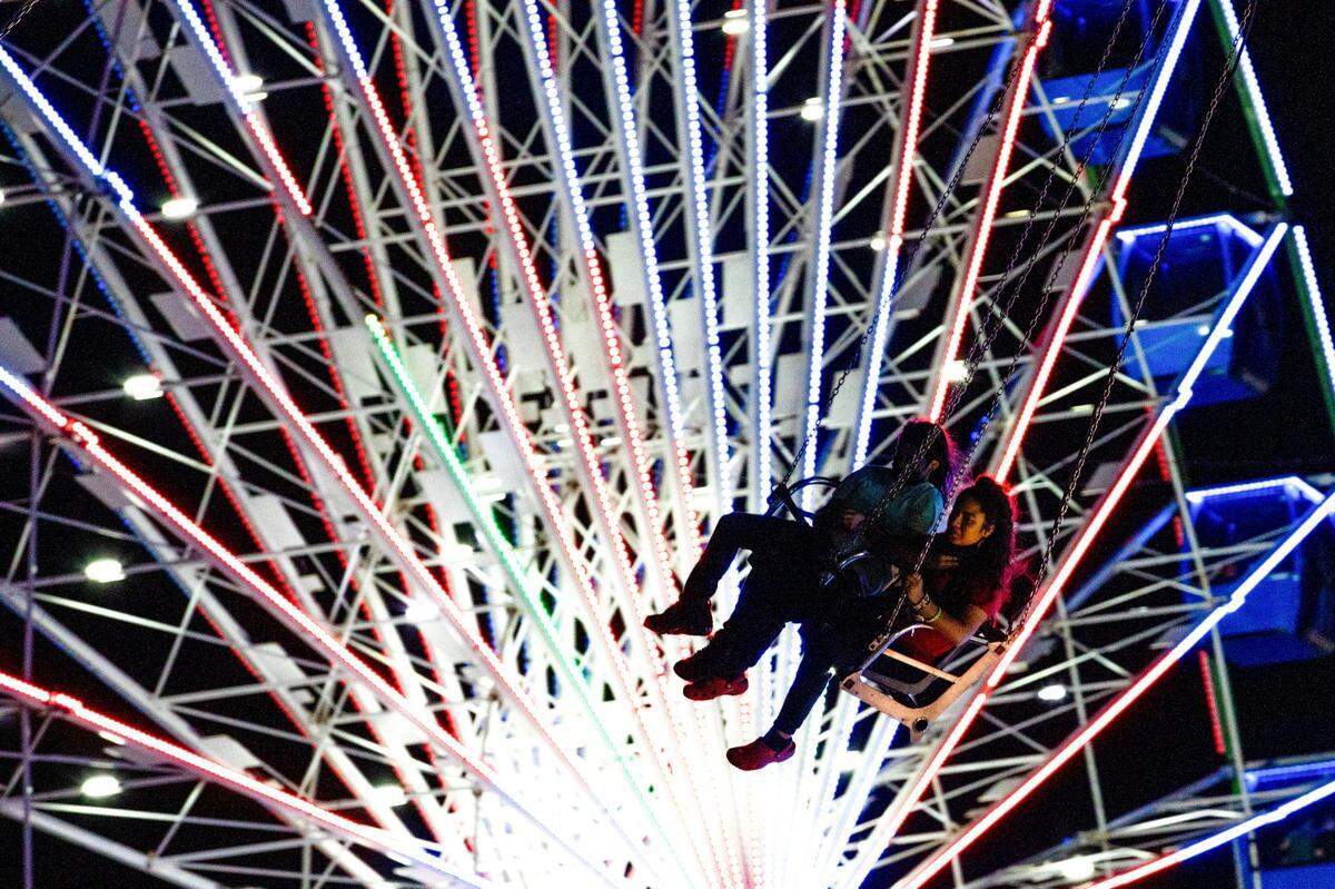 Patrons enjoy the swing ride as the Ferris Wheel spins in the background at Santa’s Enchanted Forest in Hialeah.