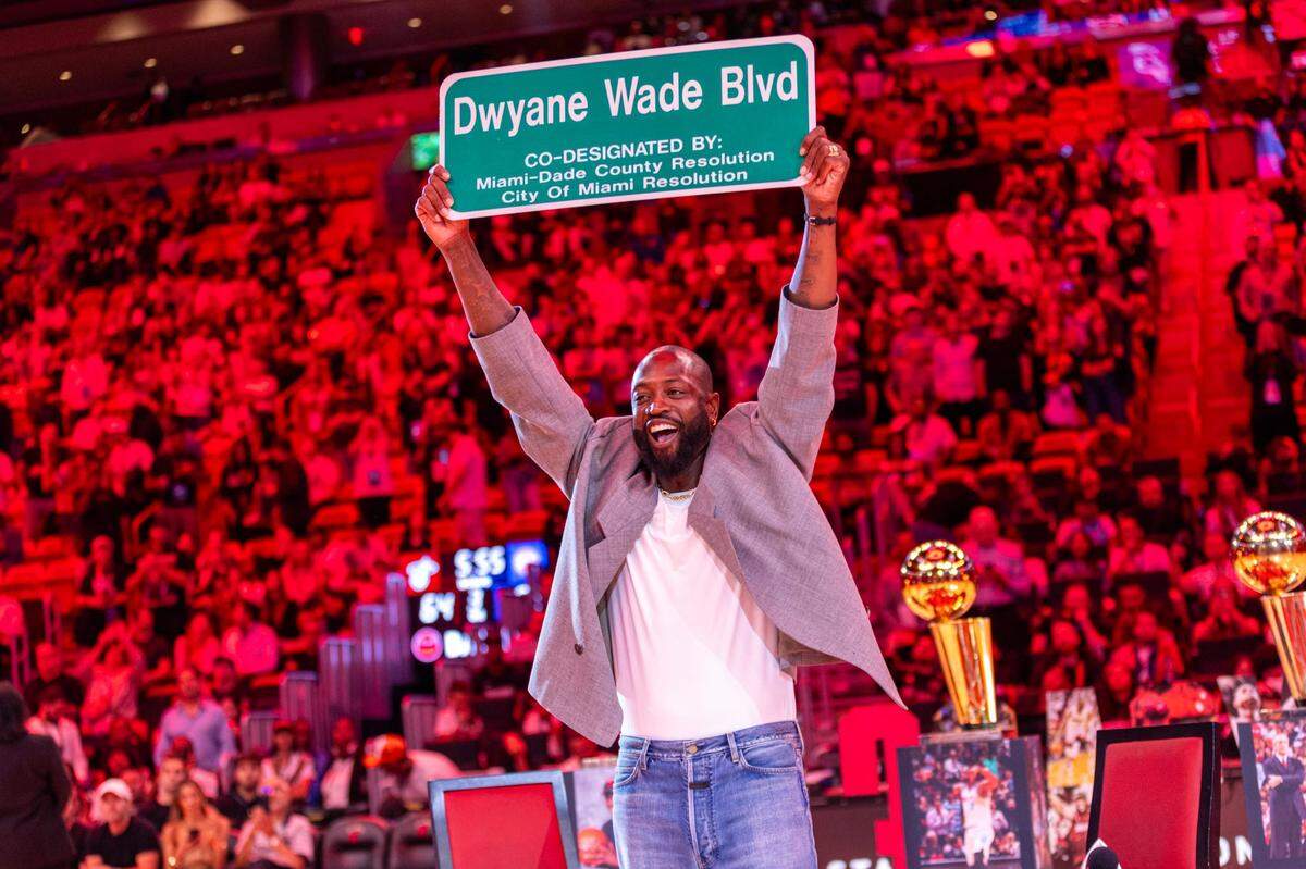Dwyane Wade sostiene el cartel de una calle perpendicular al Kaseya Center que llevará su nombre, durante una ceremonia en el medio tiempo del partido entre el Heat y los Pistons de Detroit, el 28 de octubre de 2024 en Miami, Florida.
