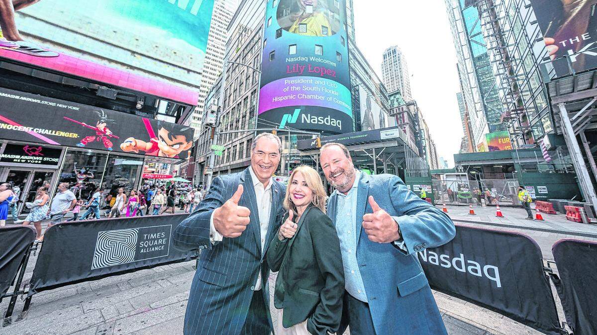 Liliam López, presidenta y fundadora de la Cámara de Comercio Hispana del Sur de la Florida, con Alex Sánchez, consejero ejecutivo del Nasdaq (izq.), y David Wicks, vicepresidente del Nasdaq (der.), frente a la pantalla de Nasdaq en Time Square, Nueva York, que ofreció un reconocimiento a López, el 25 de junio.