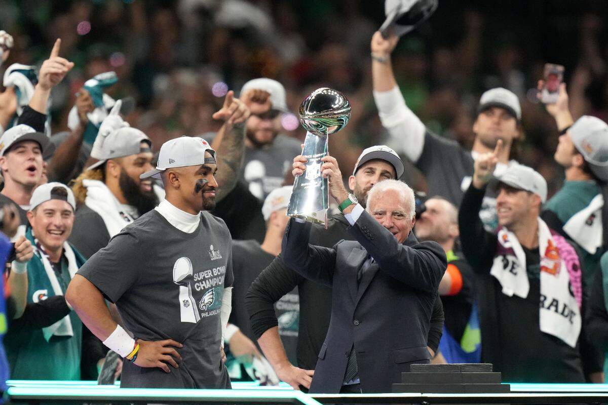 El dueño de los Eagles de Filadelfia Jeffrey Lurie levanta el trofeo Vince Lombardi tras el triunfo de su equipo ante los Chiefs de Kansas City en el Super Bowl LIX, celebrado el 9 de febrero de 2025 en Nueva Orleans. A la izquierda el quarterback Jalen Hurts.