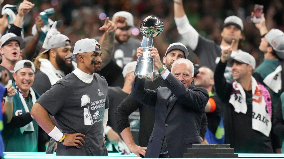 El dueño de los Eagles de Filadelfia Jeffrey Lurie levanta el trofeo Vince Lombardi tras el triunfo de su equipo ante los Chiefs de Kansas City en el Super Bowl LIX, celebrado el 9 de febrero de 2025 en Nueva Orleans. A la izquierda el quarterback Jalen Hurts.