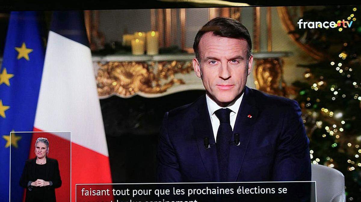 This photograph show a television screen broadcasting France's President Emmanuel Macron delivering his New Year wishes during an address to the nation from the Elysee Palace, in Paris, on December 31, 2025. (Photo by Dimitar DILKOFF / AFP via Getty Images)
