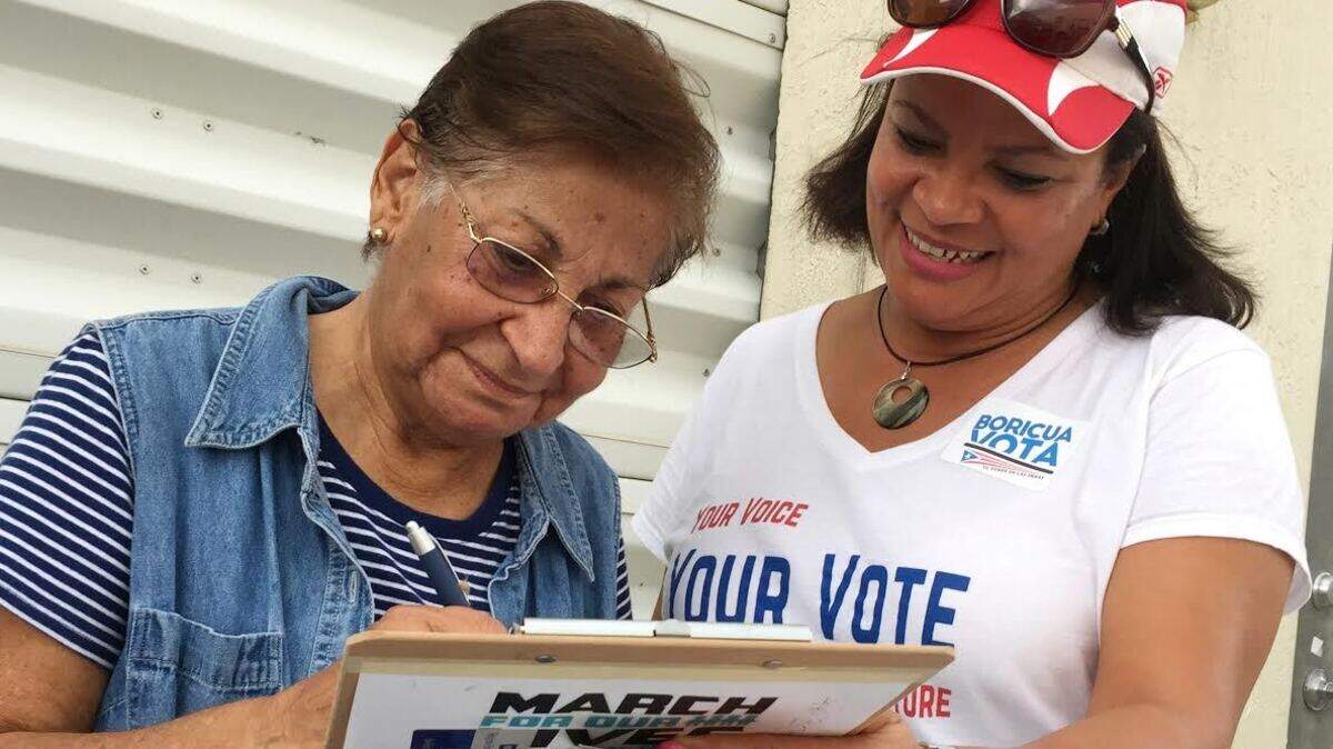 Marisol Zenteno (der.), de la Liga de Mujeres Votantes, ayuda a inscribirse en el registro electoral a Aida Merced López, quien se mudó de Puerto Rico a Miami en abril del 2017, antes que el huracán María devastara la isla, durante una jornada de inscripciones el 8 de abril del 2018 en Kendall, Florida.