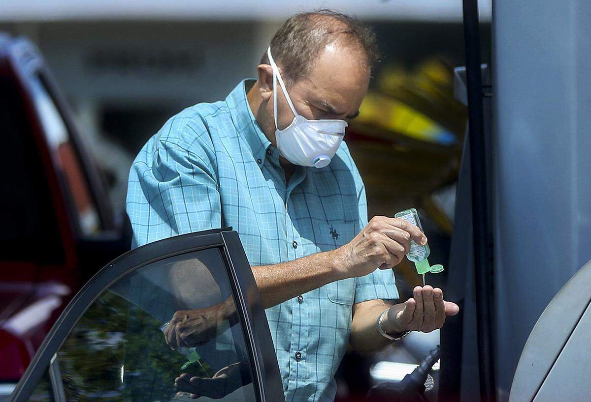 Un cliente se cubre la cara con una máscara y usa desinfectante de manos para protegerse contra COVID-19 en una estación de servicio Chevron en West Miami el miércoles, abril de 2020.