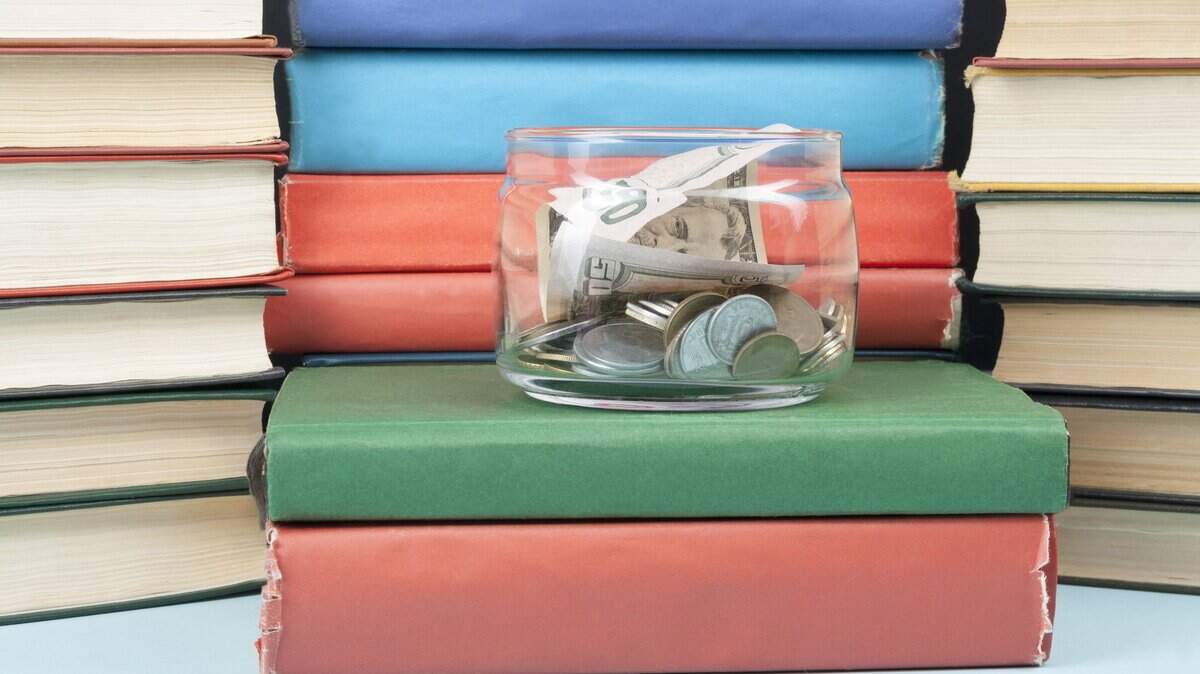 Money in glass jar and stack of books on wooden table.Concept of funding education.