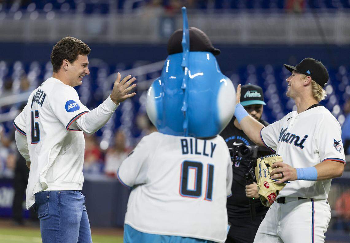 El quarterback cubanoamericano Fernando Mendoza (izq.) comparte con el jardinero Kyle Stowers tras lanzar la primera bola ceremonial antes del juego entre los Marlins y los Cardenales, el martes en el loanDepot Park de Miami.