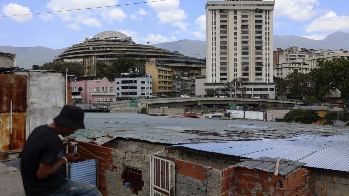 Un hombre se sienta sobre un techo en los alrededores de El Helicoide (al fondo), una instalación y prisión que alberga tanto a presos comunes como a presos políticos del Servicio Bolivariano de Inteligencia Nacional (SEBIN), en Caracas, el 26 de febrero de 2026.