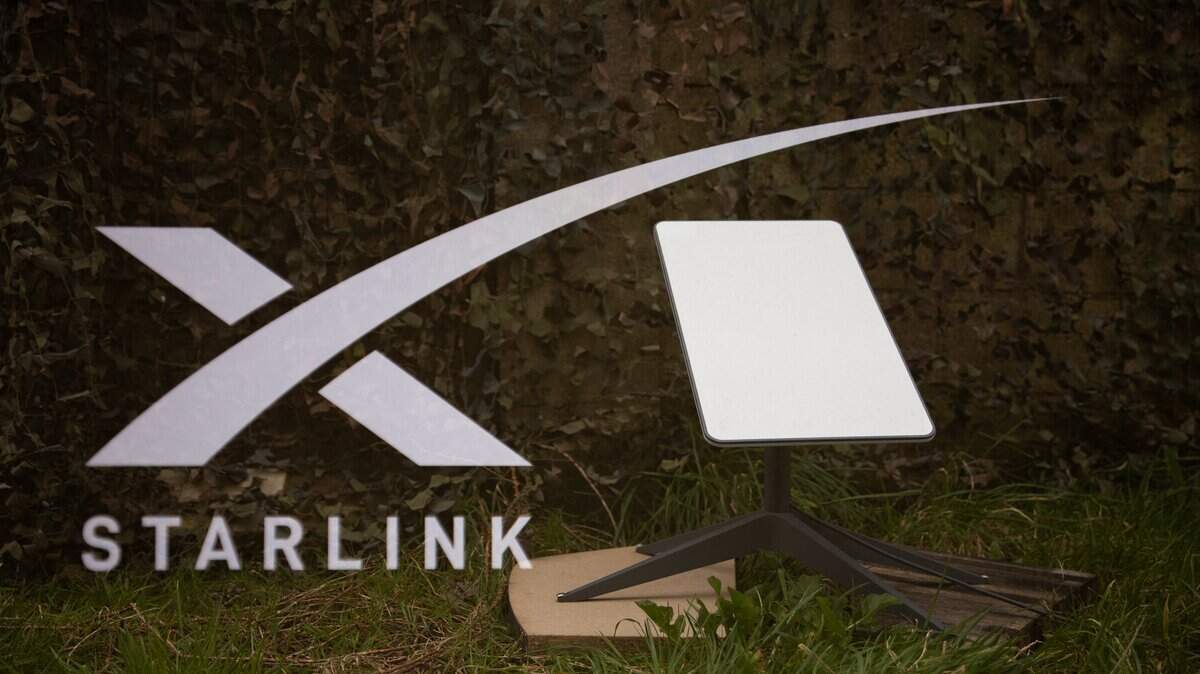 Fotografía de doble exposición del logotipo de Starlink y una antena satelital en tierra, frente a una red de camuflaje militar en Kerlouan, en Bretaña (Francia), el 1 de marzo de 2025.