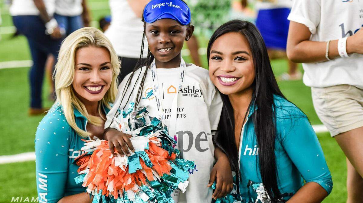 Dos cheerleaders de los Dolphins posan con una niña en la Fiesta del Pijama, la actividad que organiza el equipo de Miami en su programa de ayuda a la comunidad.