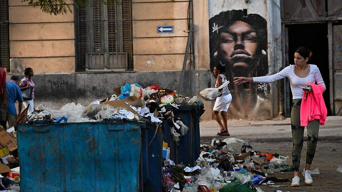 A woman throws a bag over garbage on a street in Havana on December 4, 2025. Twenty-one children are among 33 people who have died in Cuba of the mosquito-borne chikungunya and dengue viruses since July, authorities said Monday. Health authorities admitted that an epidemic is affecting the entire country, as the accumulation of garbage, stagnant water, and blackouts have created ideal conditions for the proliferation of mosquitoes transmitting the viruses. (Photo by YAMIL LAGE / AFP via Getty Images)