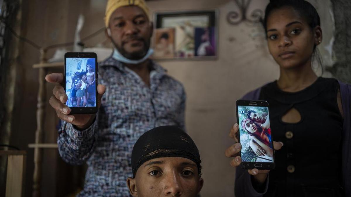 Odlanier Santiago Rodríguez, al centro, quien fue acusado de participar en las protestas de julio del año pasado y fue liberado tras 22 días en prisión, posa para una fotografía junto con su tío y su nuera, mientras muestran fotos de los tres hijos de Román que aún permanecen detenidos el 19 de enero de 2022 (AP Foto/Ramón Espinosa)