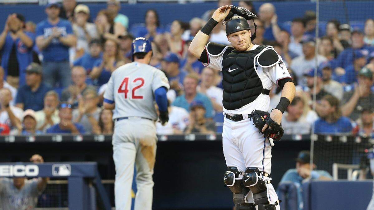 El receptor de los Marlins Chad Wallach observa como Ben Zobrist anota por los Cachorros en el primer inning, en el partido efectuado el 15 de abril de 2019 en Miami.