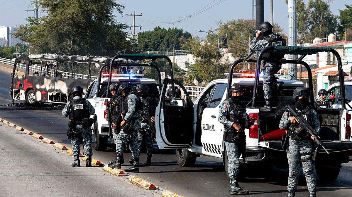 Miembros de la Guardia Nacional patrullan  cerca de un autobús quemado por grupos del crimen organizado en respuesta a la muerte de Nemesio Oseguera, alias “El Mencho”, jefe del poderoso cártel Jalisco Nueva Generación (CJNG), abatido por el ejercito, el 22 de febrero de 2026 en Jalisco, México. 