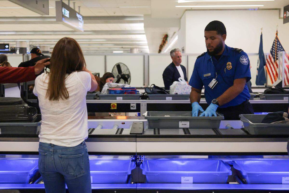 Un agente de la TSA le indica a una viajera que coloque su equipaje y pertenencias en una bandeja en una fila con un sistema automatizado de devolución de bandejas durante un control de seguridad estándar en el punto de control 2 del Aeropuerto Internacional de Miami el martes 25 de noviembre en Miami, Florida.