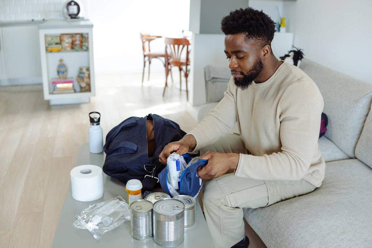 Un hombre organiza en una bolsa artículos esenciales de emergencia, incluyendo alimentos enlatados, artículos de tocador y suministros. Es recomendable reunir los suministros en un kit para huracanes antes de la llegada de una tormenta. 