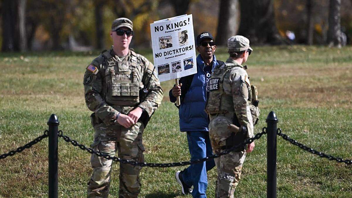 A protestor walks by members of the National Guard during the kick off event for a "Trump Must Go" protest near the Washington Monument in Washington, DC, on November 5, 2025, marking the first anniversary of Donald Trump's election to a second term. (Photo by ANDREW CABALLERO-REYNOLDS / AFP) (Photo by ANDREW CABALLERO-REYNOLDS/AFP via Getty Images)