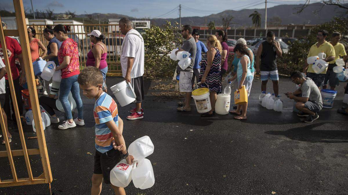 Personas en Puerto Rico hacen fila para rellenar envases con agua potable en el exterior de una Estación de Policía en Juncos, Puerto Rico, después de que el huracán María azotara la isla en septiembre de 2017.