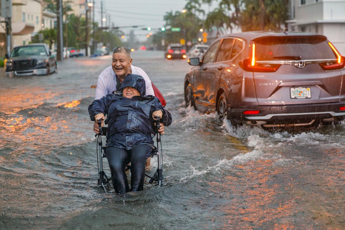 Víctor Corone, de 66 años, empuja a su esposa María Díaz, de 64 años, en silla de ruedas a través de más de un pie de agua de inundación en la calle 84 en Miami Beach el miércoles 12 de junio de 2024. Díaz tenía una cita con el médico y tuvieron que abandonar el auto en el estacionamiento de Collins Ave y caminar más de 20 minutos para llegar a casa.