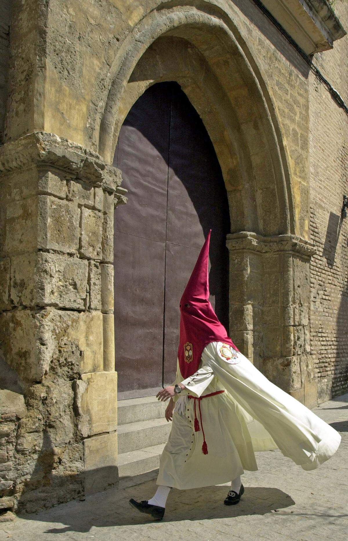 Un nazareno pasa junto a una de las puertas de la Iglesia de San Martín en Sevilla, donde la Hermandad de la Lanzada inicia su recorrido procesional.