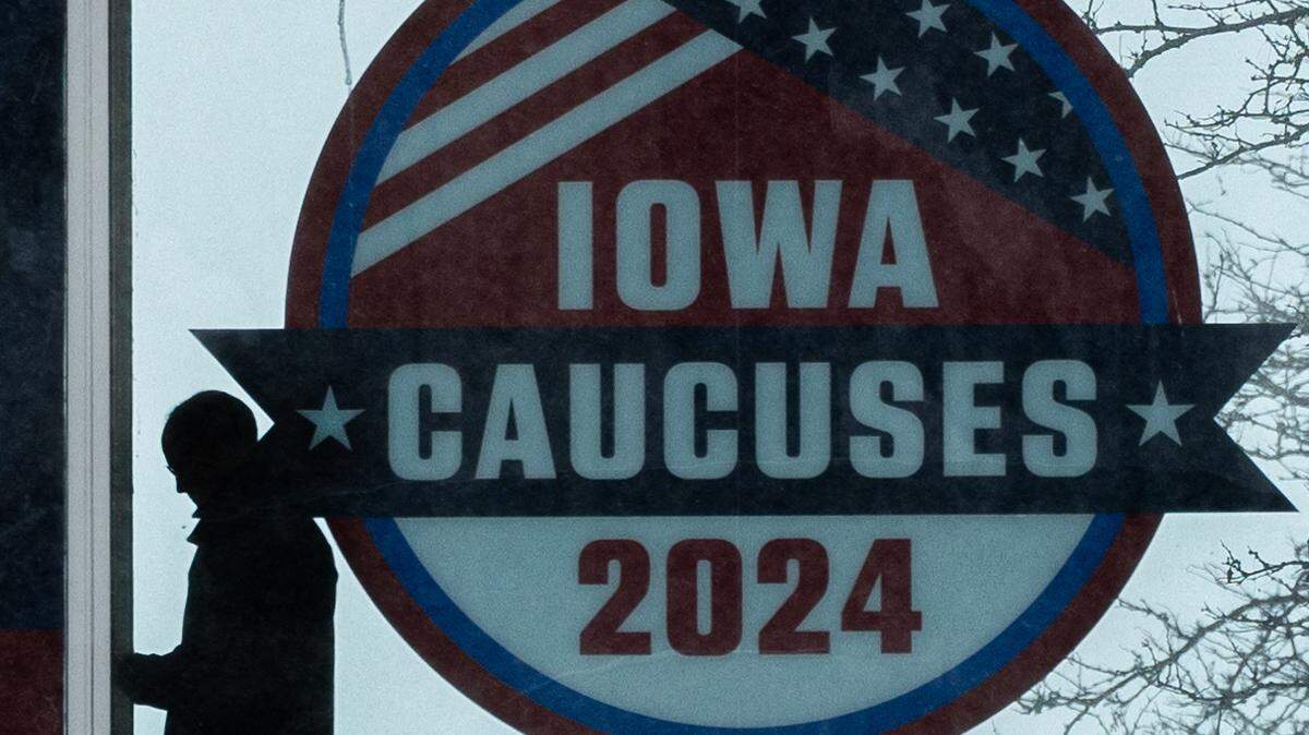 Una persona camina frente a un anuncio que promociona los “caucuses” (asambleas) de Iowa, durante una fuerte tormenta de nieve, en Des Moines, el viernes 12 de enero de 2024.